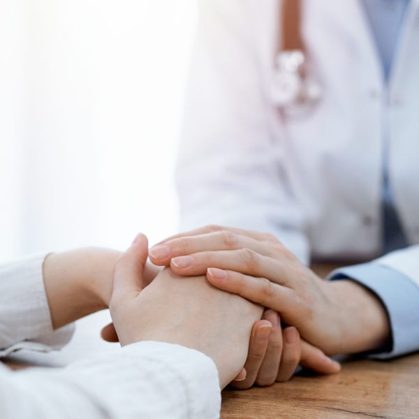 Doctor,And,Patient,Sitting,At,The,Wooden,Table,In,Clinic.